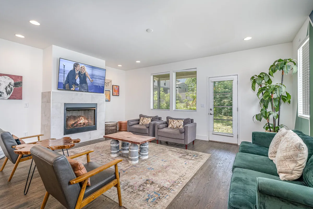 This image features a cozy living room setup with a fireplace as the centerpiece, a comfortable seating arrangement, a large television, and curated artwork. The door to the outside subtly hints at indoor-outdoor flow. The space is clearly designed for relaxing, socializing, and entertainment, all key aspects highlighted in the section.