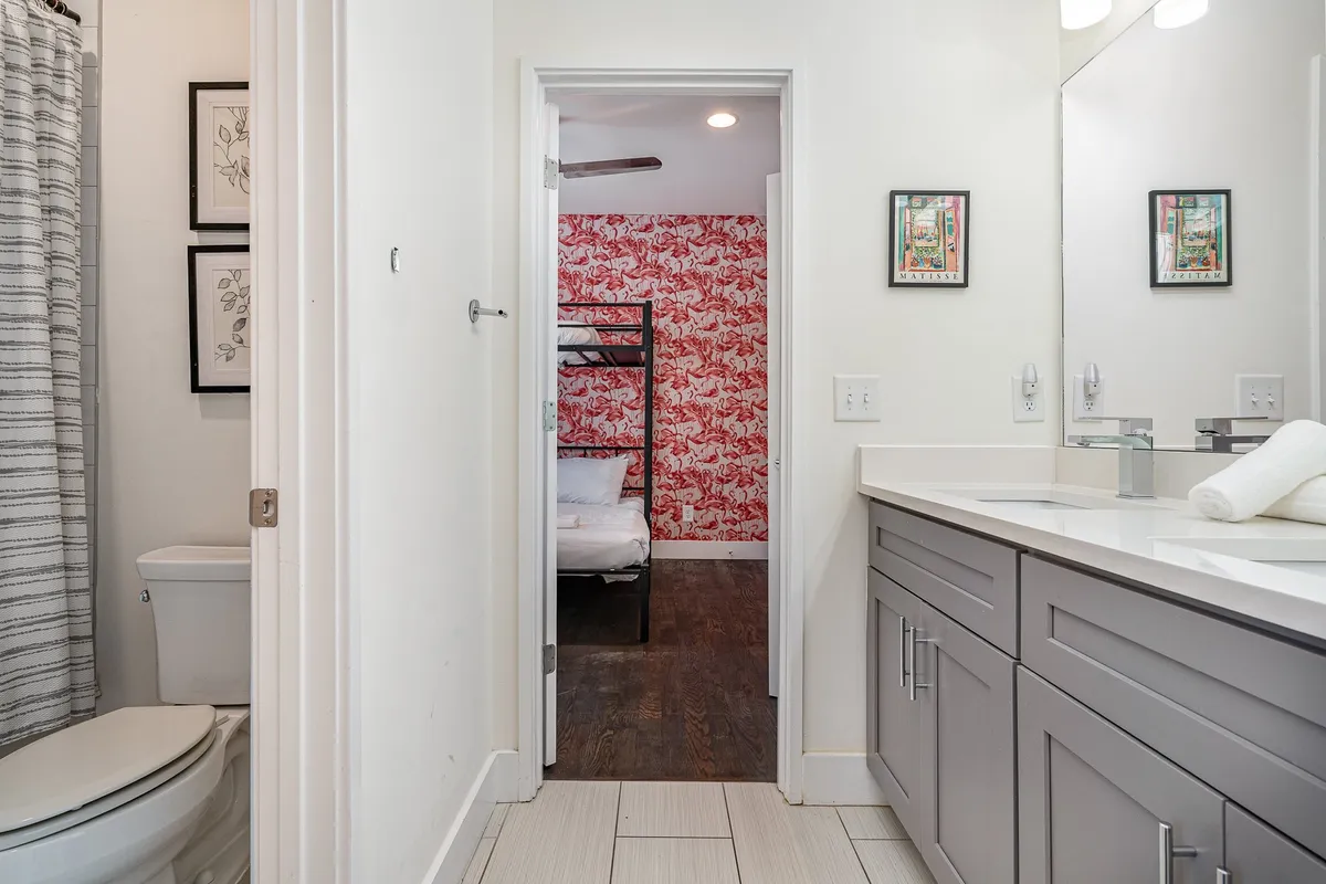 A playful, functional space displaying a vanity with sink, bunk bed accented by a decorative wall, and a doorway connecting the bunk room to a bathroom. The scene suggests a cozy and accessible environment for children or groups.