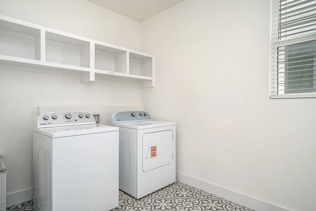 The image displays a functional and organized laundry room, featuring a washer, dryer, and neatly arranged shelves. The clean, practical setup conveys ease of use for guests needing to do laundry during their stay.
